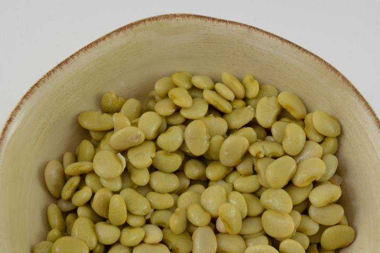 Top view of lima beans in cream colored rustic bowl with a white background.