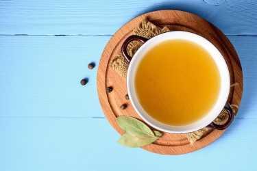A top view of a pot of Homemade Chicken Broth on a blue background.